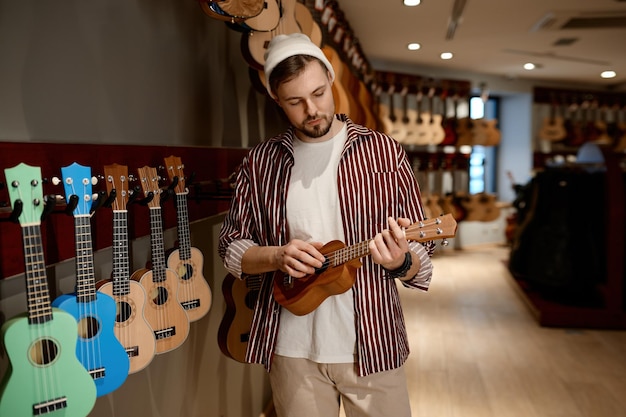 young hipster man musician buying ukulele guitar musical instrument shop store hobby business commerce concept